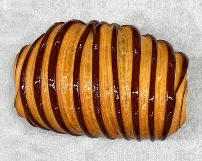 A pain au chocolat with glossy chocolate stripes, on baking parchment.